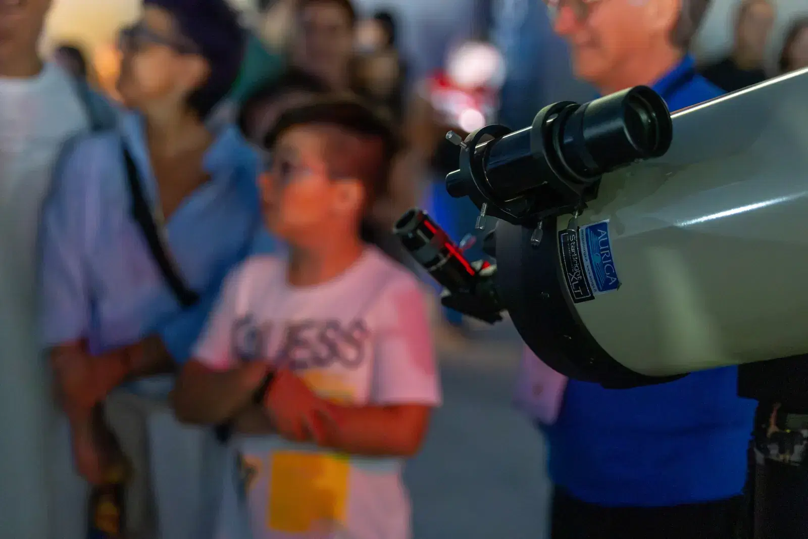 A child waits next to a white telescope, with other people around