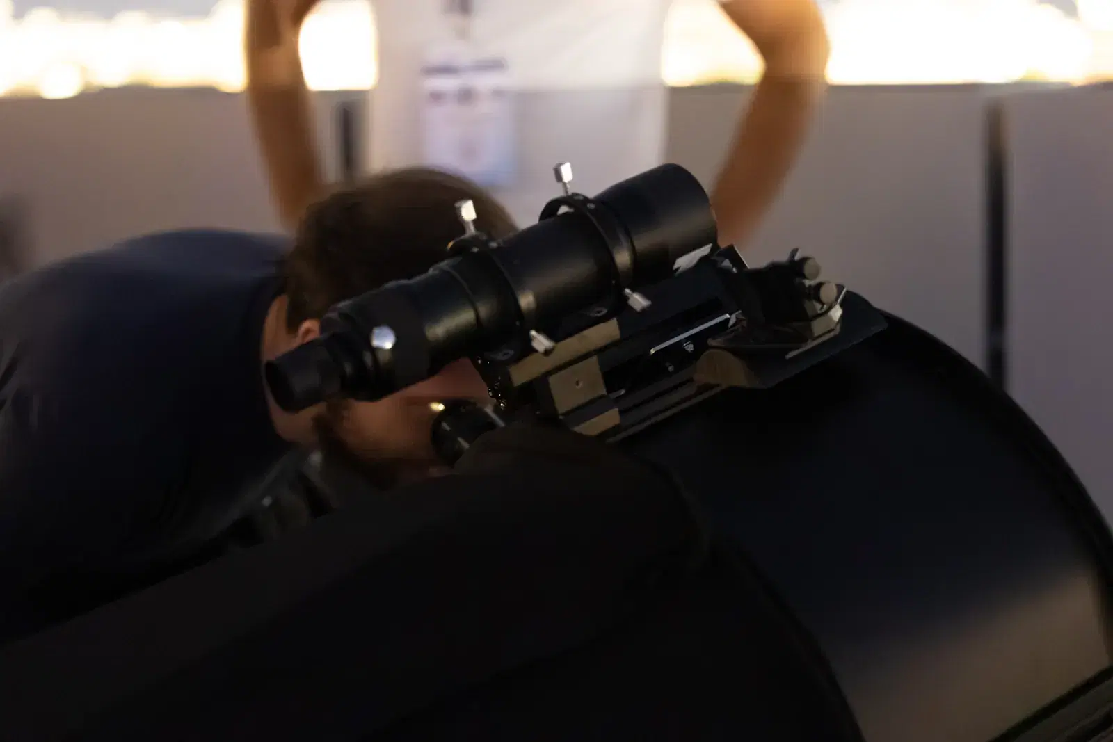 A boy bends over the eyepiece of a large black telescope, with the sky still light