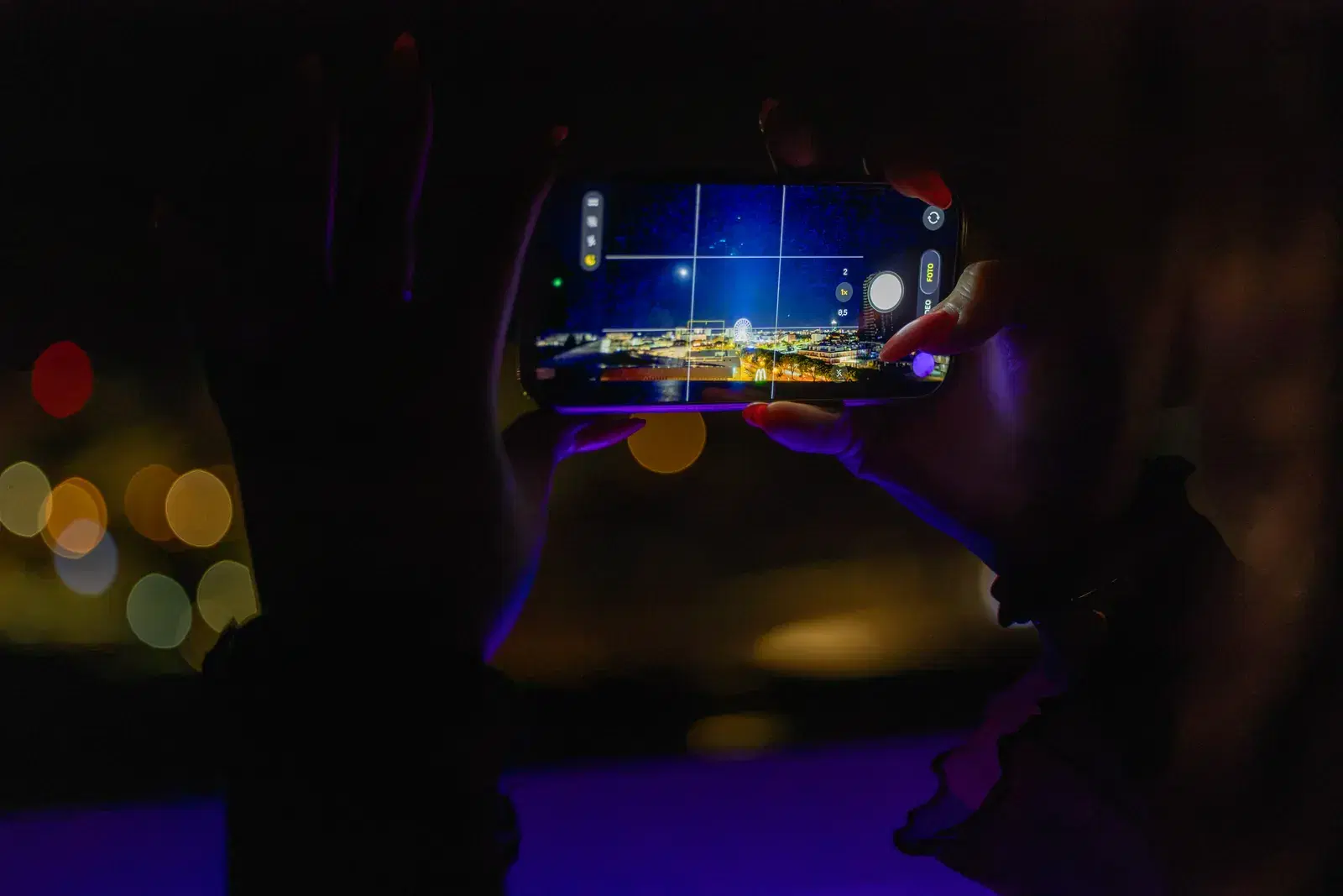 A phone frames the sky and the city lights, in the dark