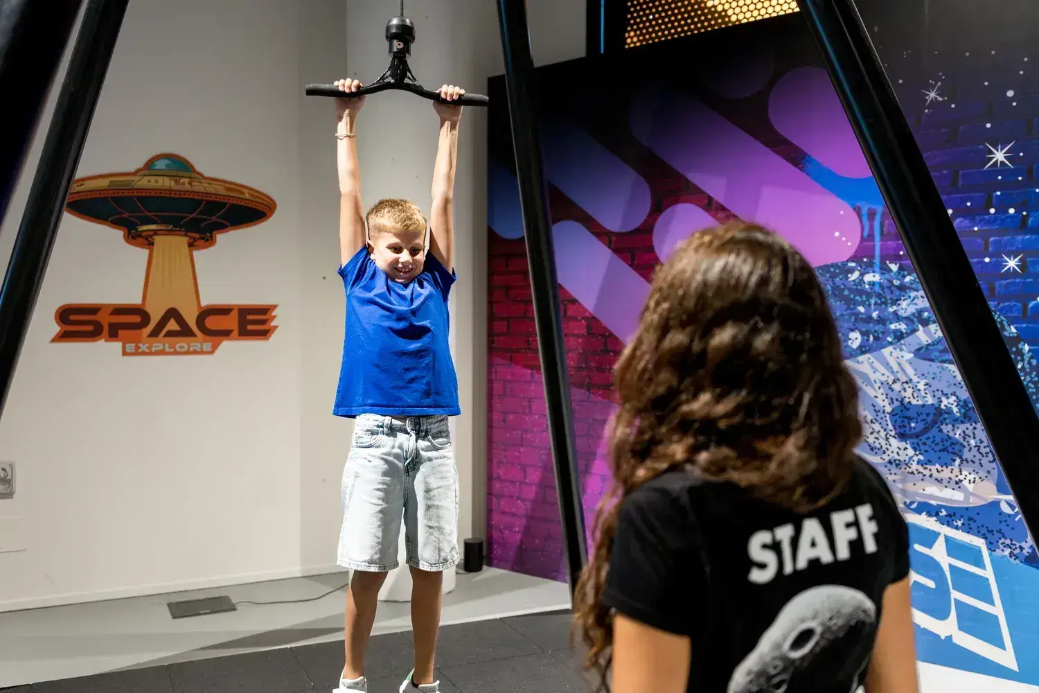 A visitor sitting at the orbital pulleys station lifts herself by pulling the rope, with an operator beside her