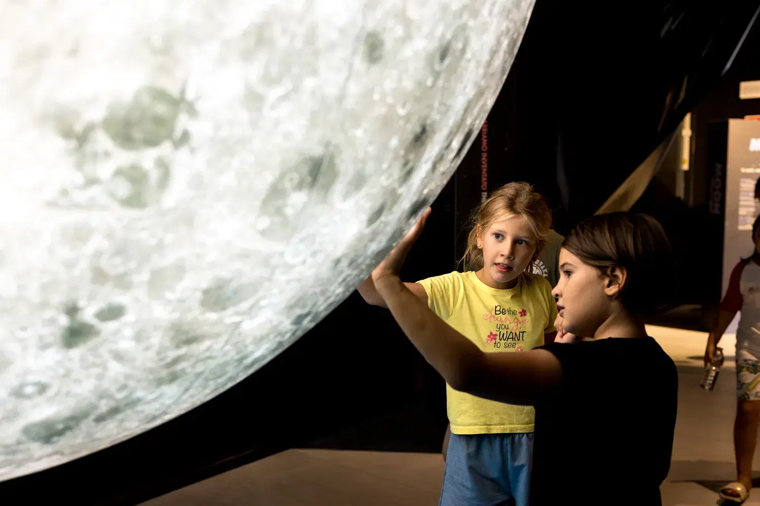 Two girls reach out to touch the great suspended Moon