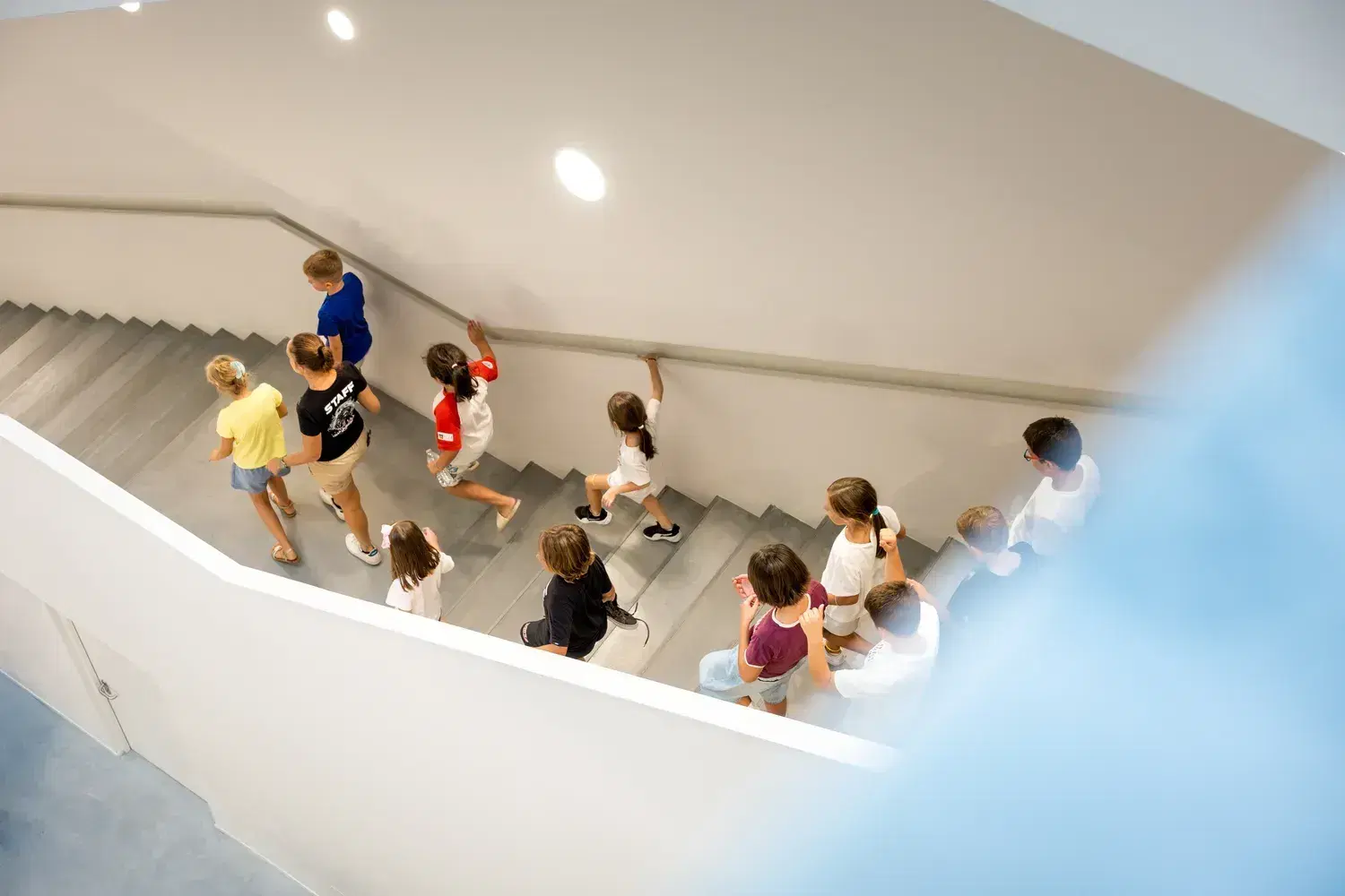 A school group climbs the white staircase of the JMuseo, seen from above