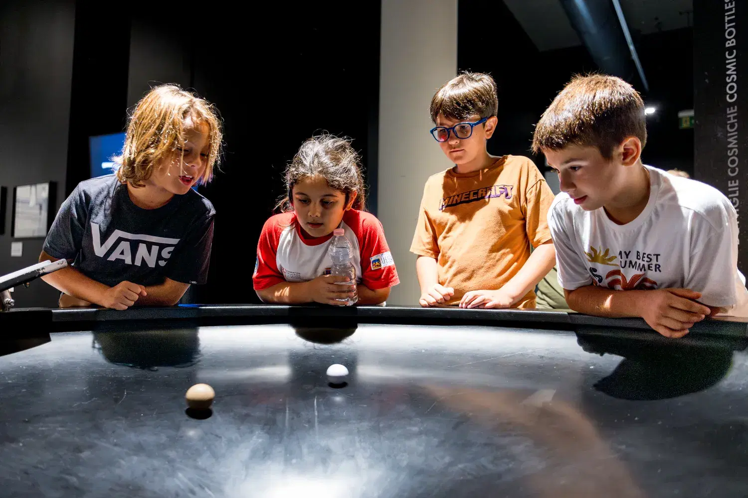 Four children watch an experiment on a dark table