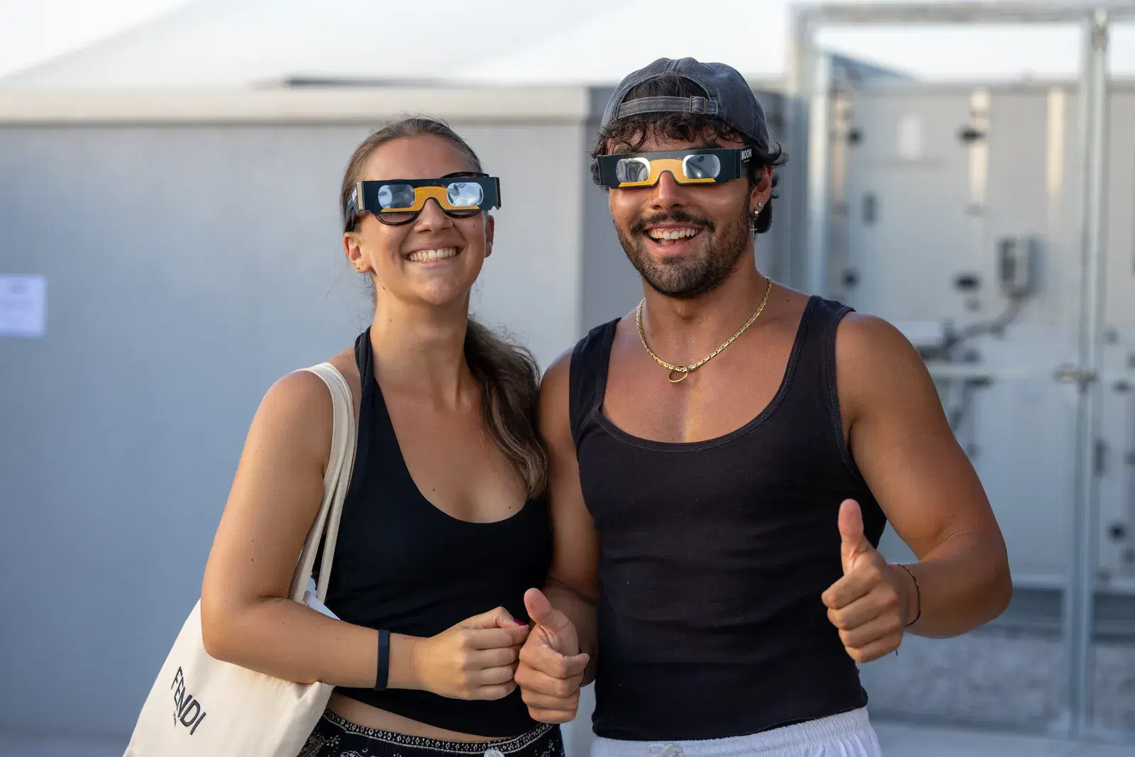 Due visitatori sorridenti con gli occhiali da eclissi indossati e il pollice alzato