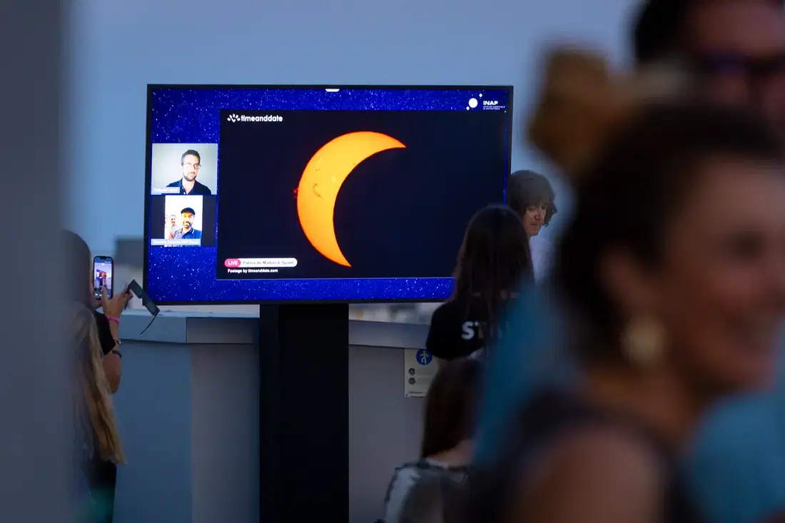 Uno schermo in terrazza mostra il Sole eclissato ripreso in diretta, con il pubblico davanti