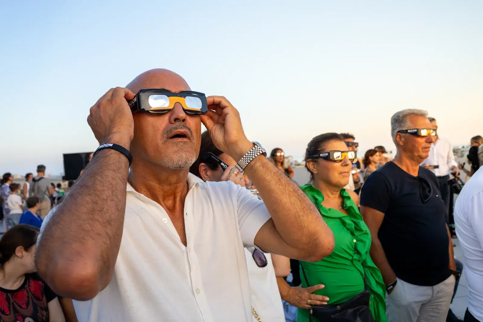 Un visitatore si sistema gli occhiali da eclissi guardando verso il Sole, dietro di lui altre persone osservano