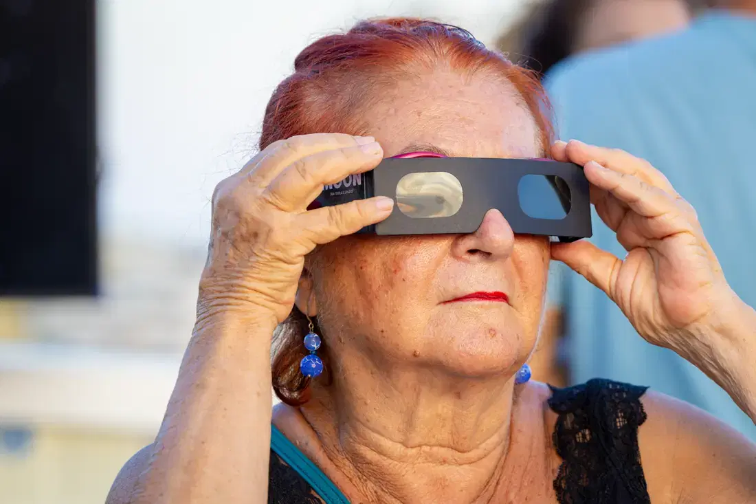 Una signora tiene gli occhiali da eclissi davanti agli occhi con entrambe le mani