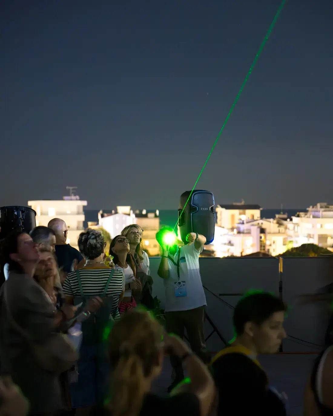 Un astrofilo indica una costellazione con un puntatore laser verde davanti al pubblico sulla terrazza