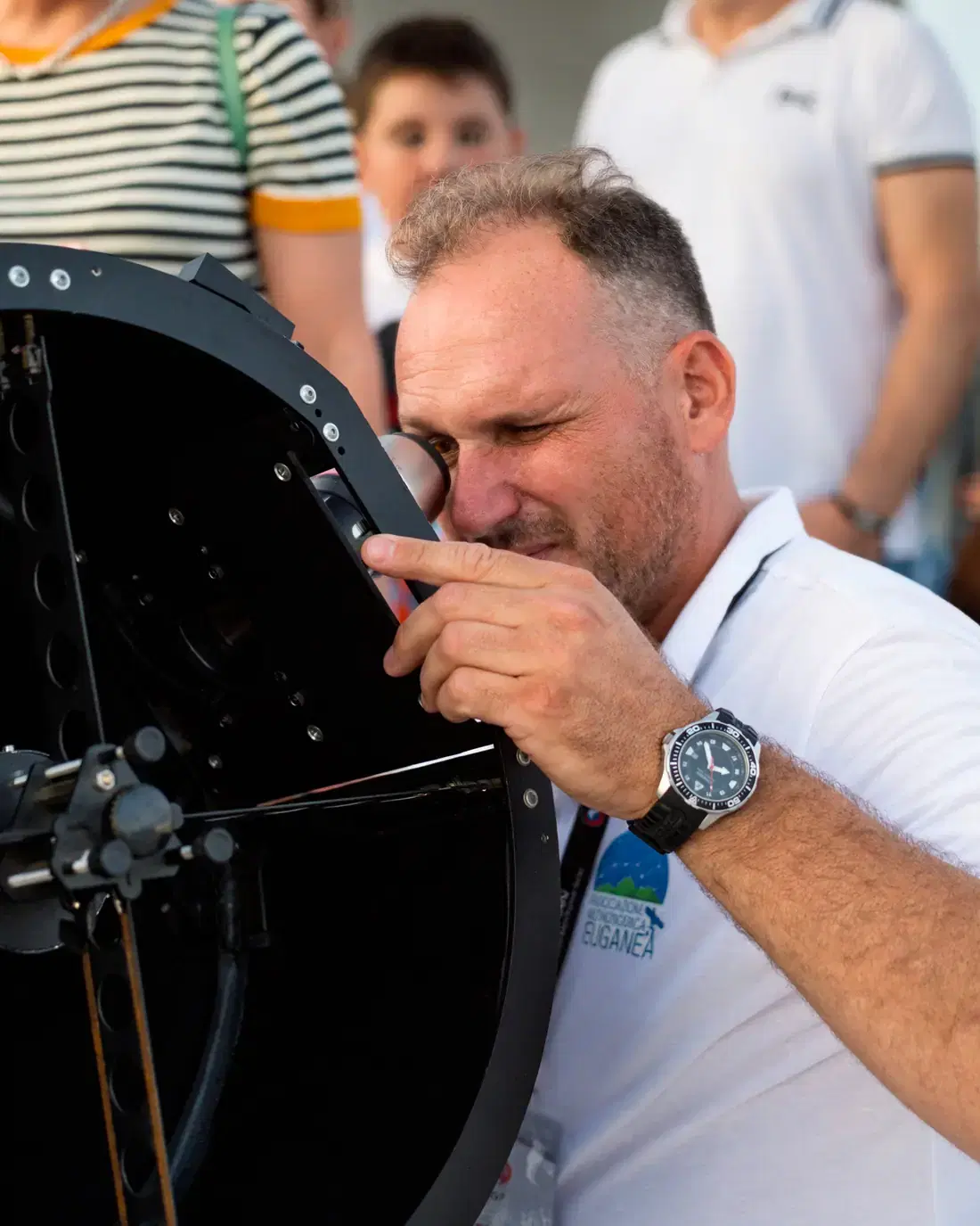 Un socio degli astrofili osserva all'oculare di un grande telescopio newtoniano, con il pubblico alle spalle