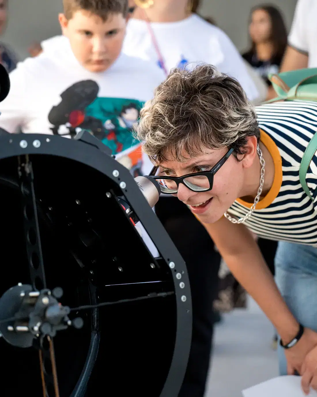 Una visitatrice guarda nell'oculare del telescopio mentre un ragazzo aspetta il proprio turno