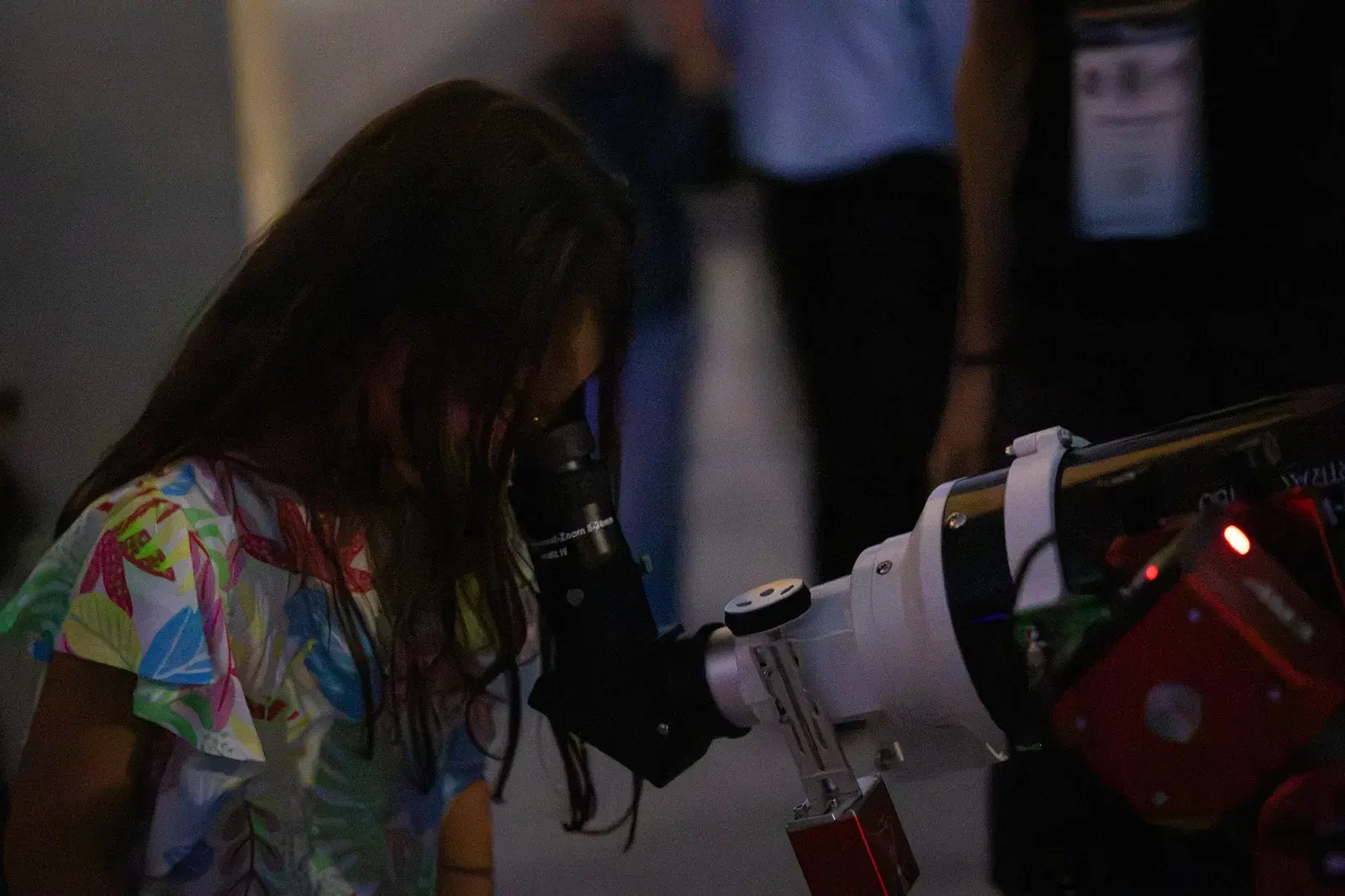 Una bambina con la maglietta a fiori si china sull'oculare di un telescopio rifrattore