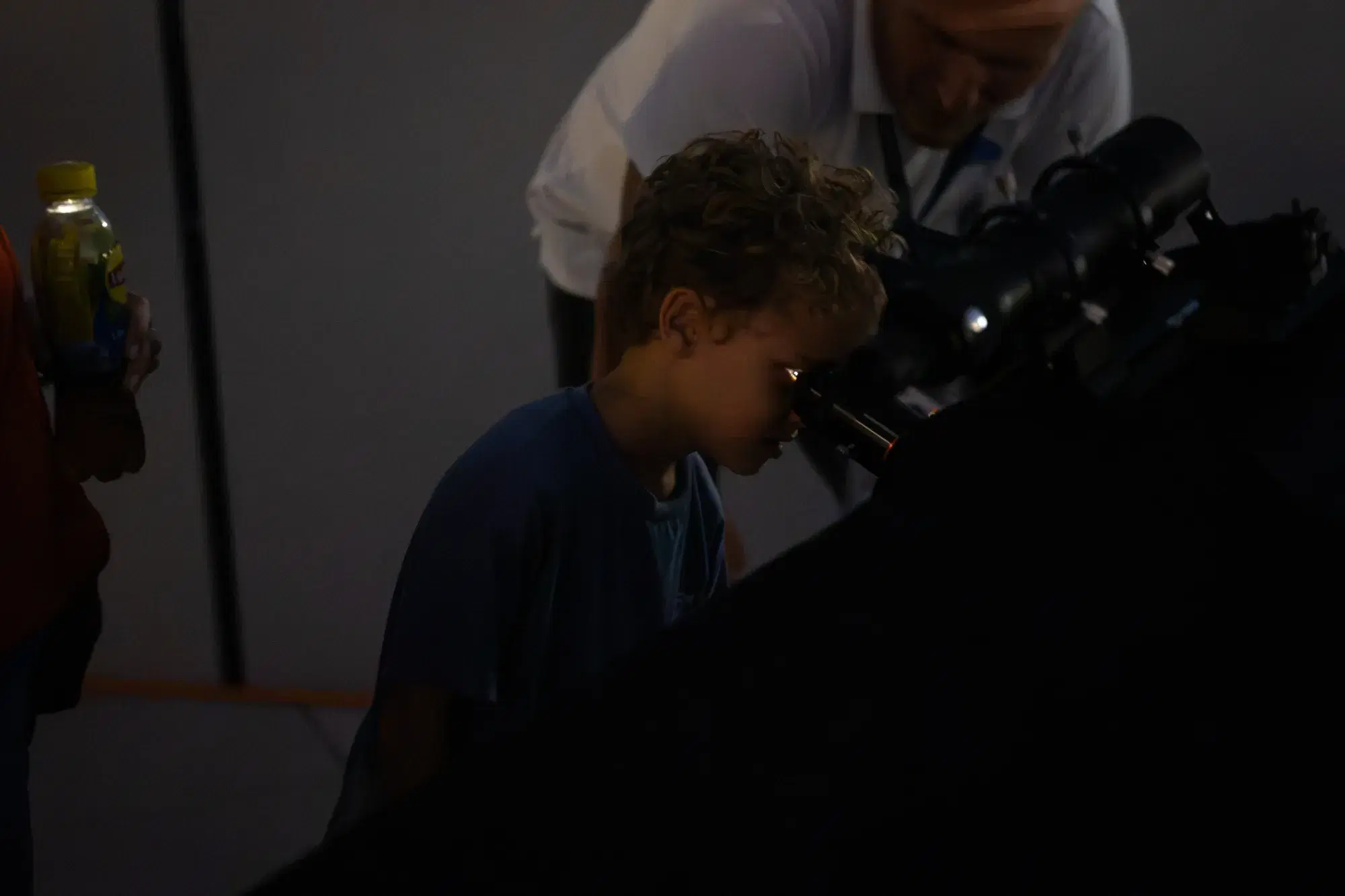 Un bambino guarda nell'oculare del telescopio mentre un astrofilo lo accompagna tenendo lo strumento