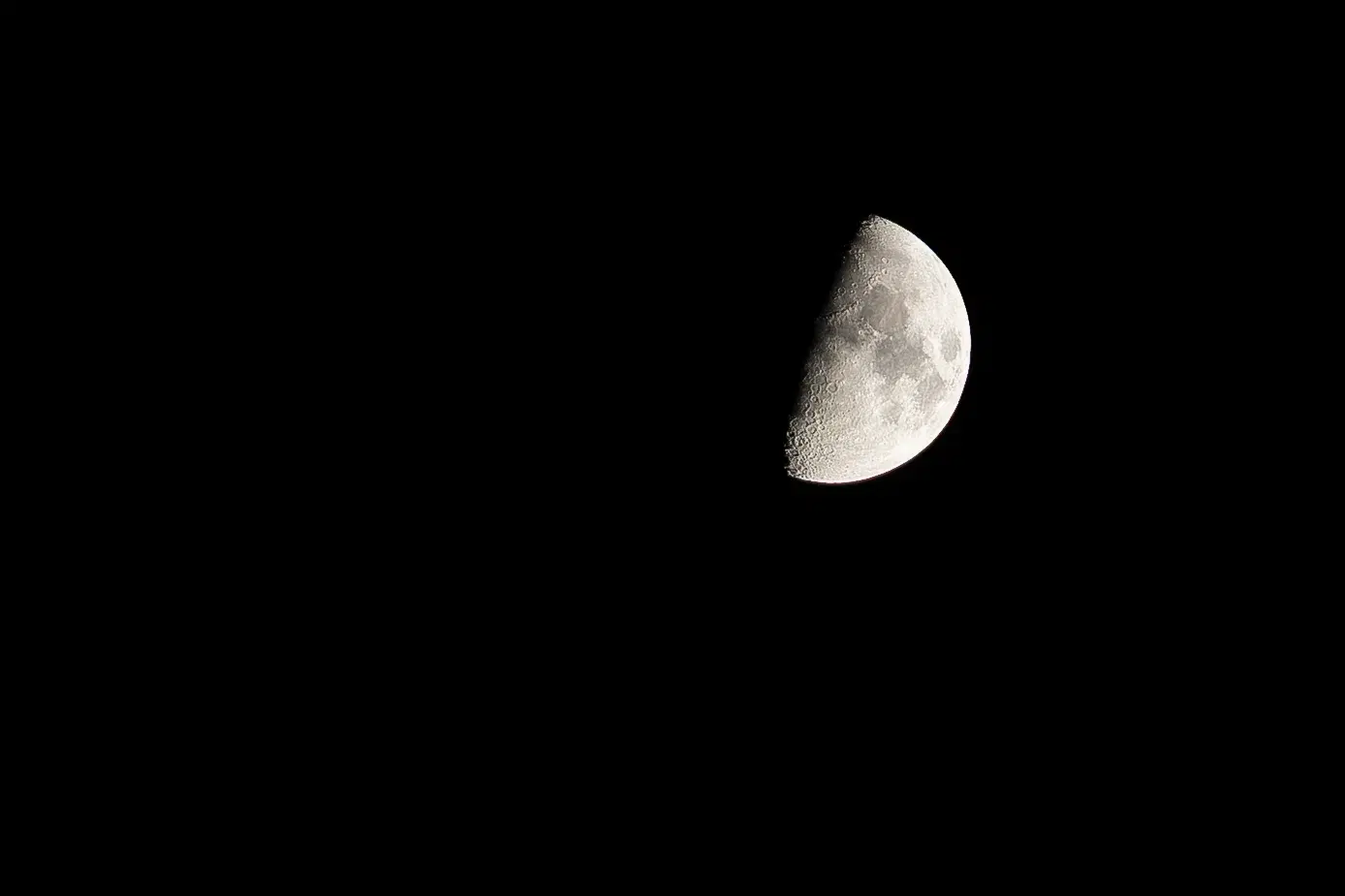 La Luna al primo quarto nel cielo nero, con i crateri in rilievo lungo la linea d'ombra