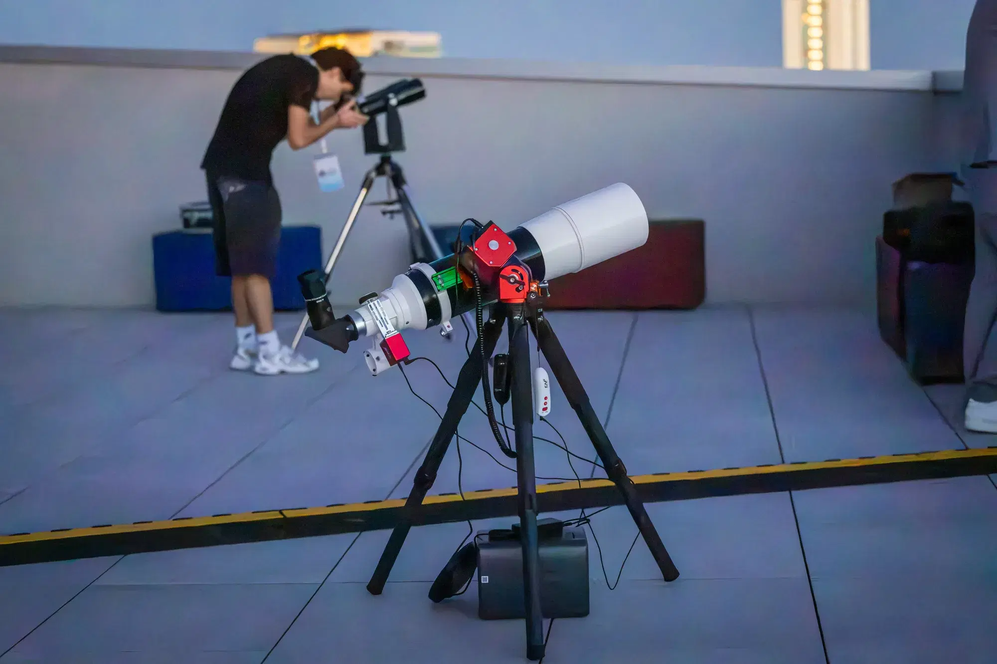 Un ragazzo si china sul telescopio rifrattore montato sulla terrazza, con il cielo ancora chiaro