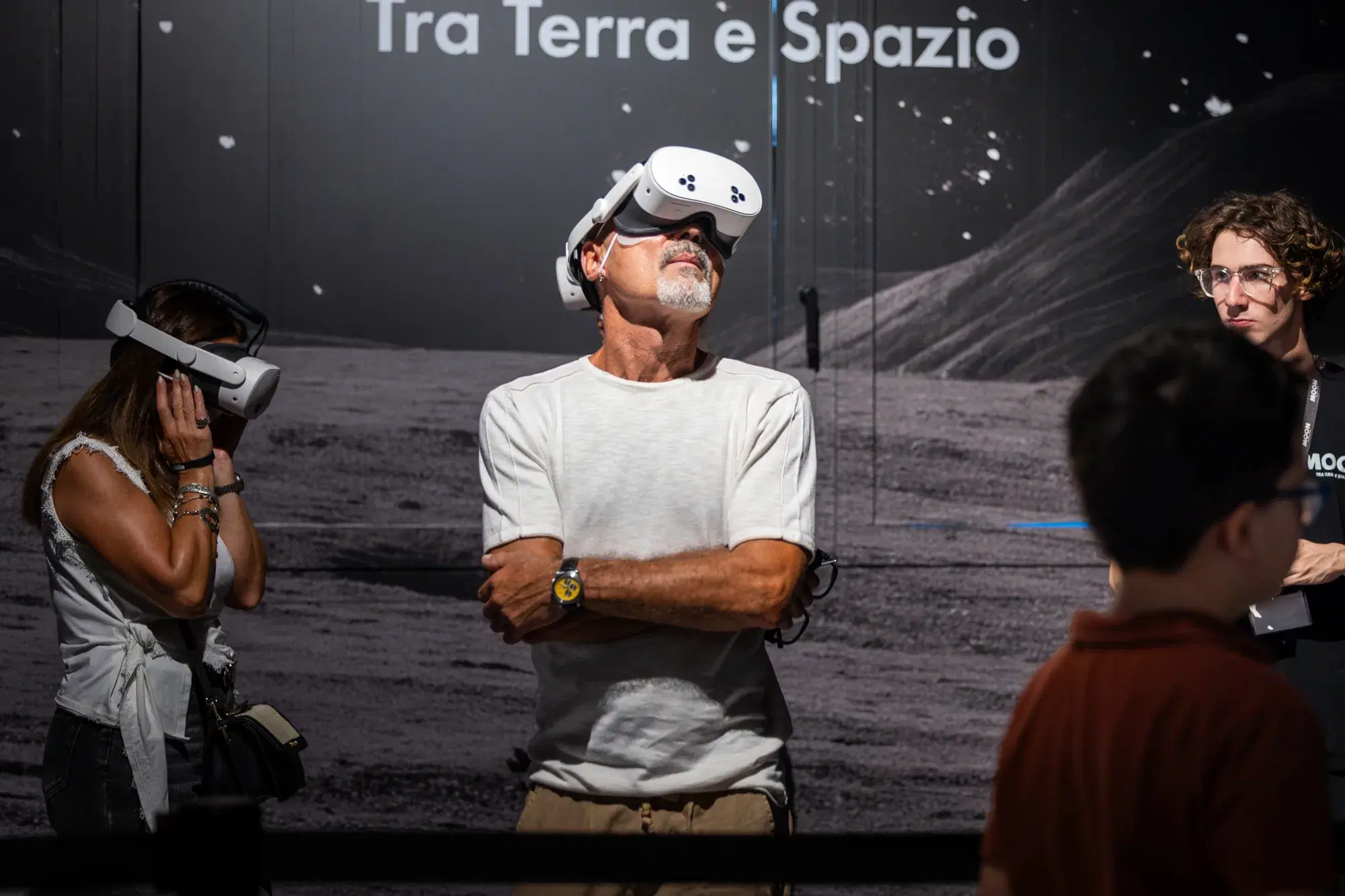 Un visitatore con il visore indossato, in piedi davanti alla grande parete lunare della mostra, con altre persone intorno